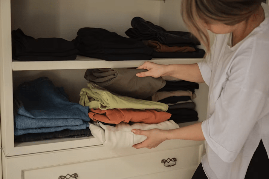 Image of a professional organizer arranging neatly folded clothes on white wardrobe shelves during a closet organizing session