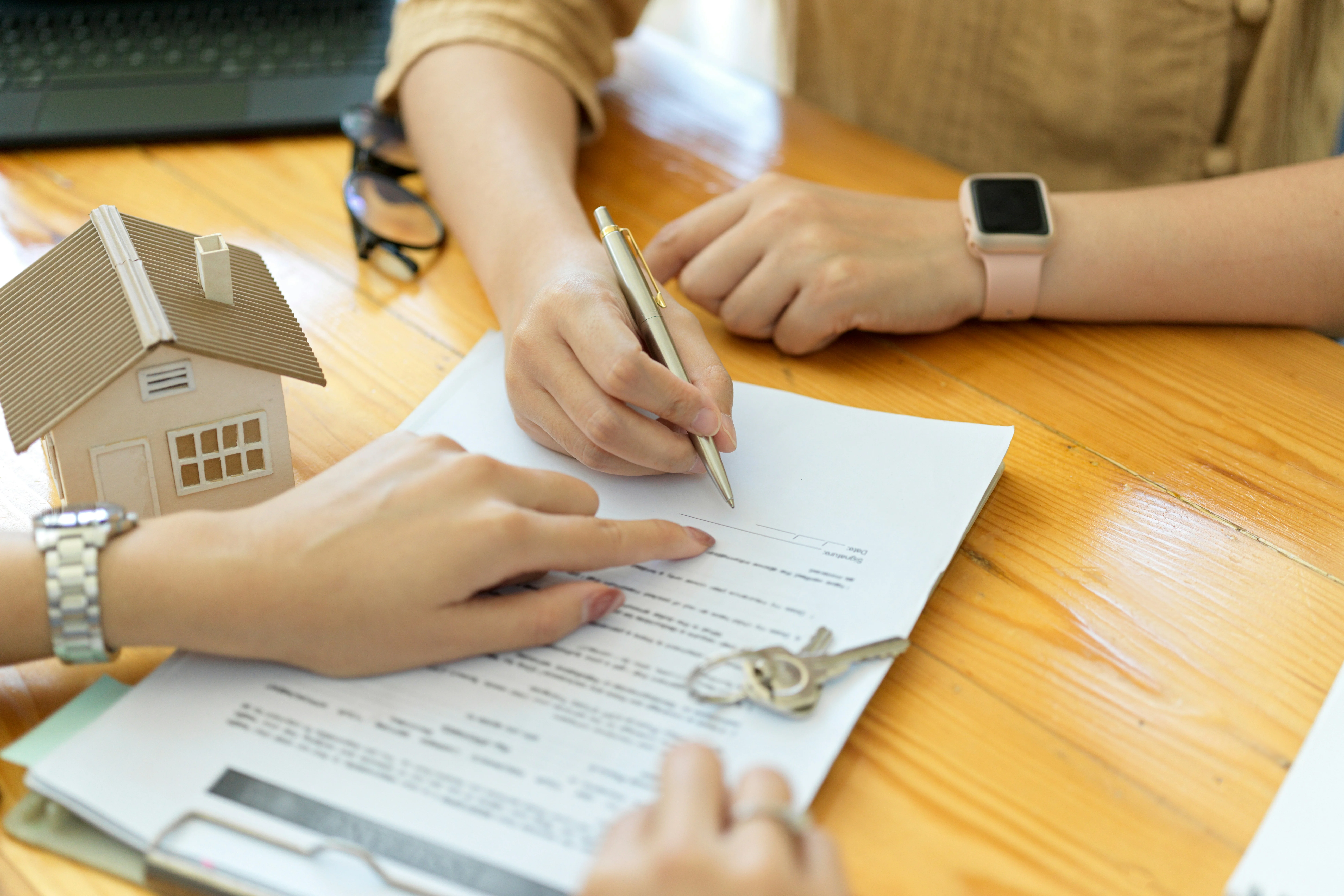 image of tenant signing rental lease agreement with house model on wooden desk