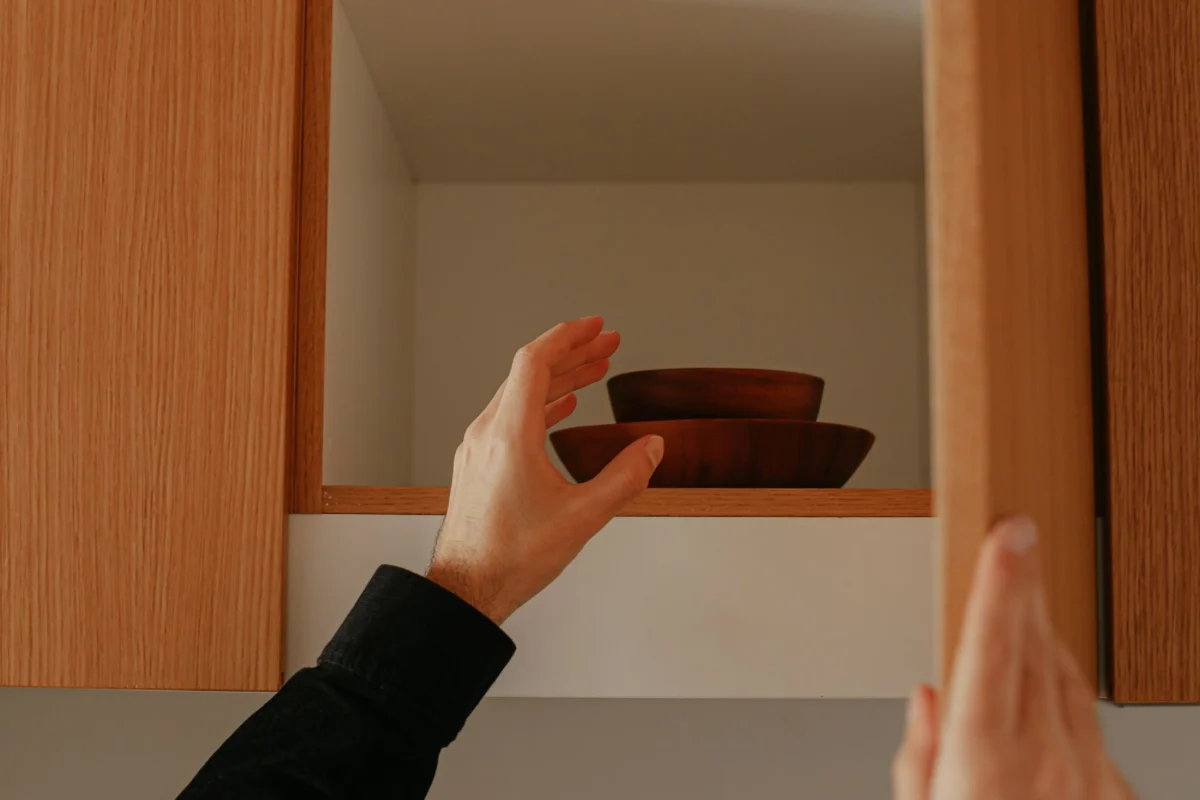 Hand placing wooden bowls in a clean kitchen cabinet after a move-in cleaning