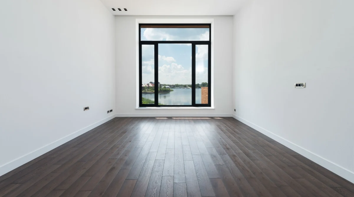 Empty room with dark wood floors and a large window, ready for cleaning