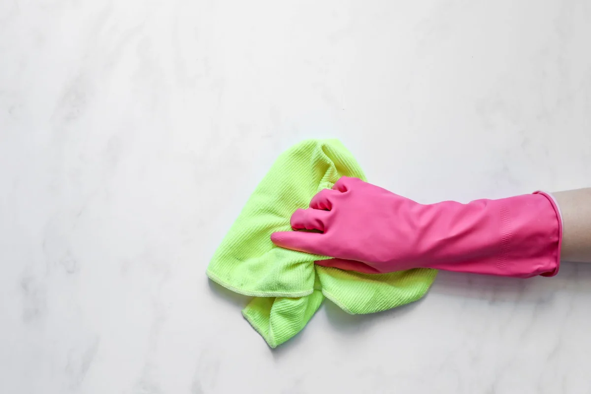 Pink rubber glove wiping a white marble counter with a green cloth
