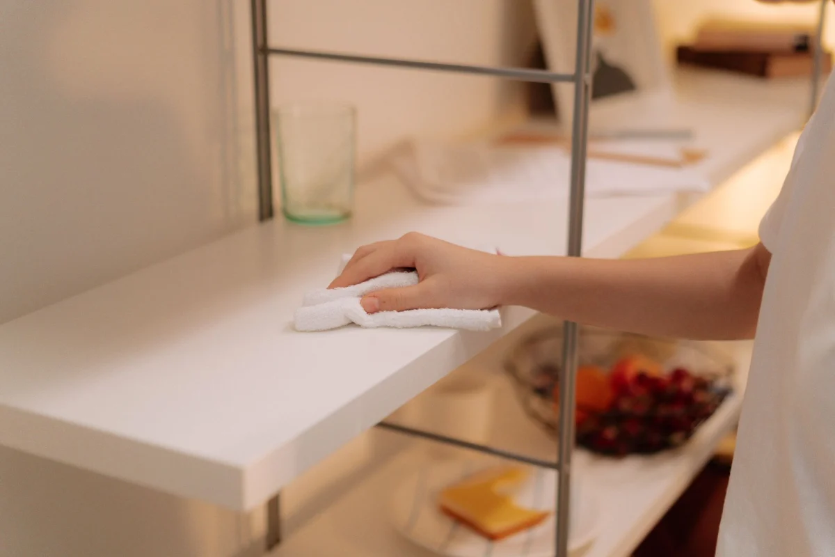 Hand wiping dust off a white shelf with a cloth