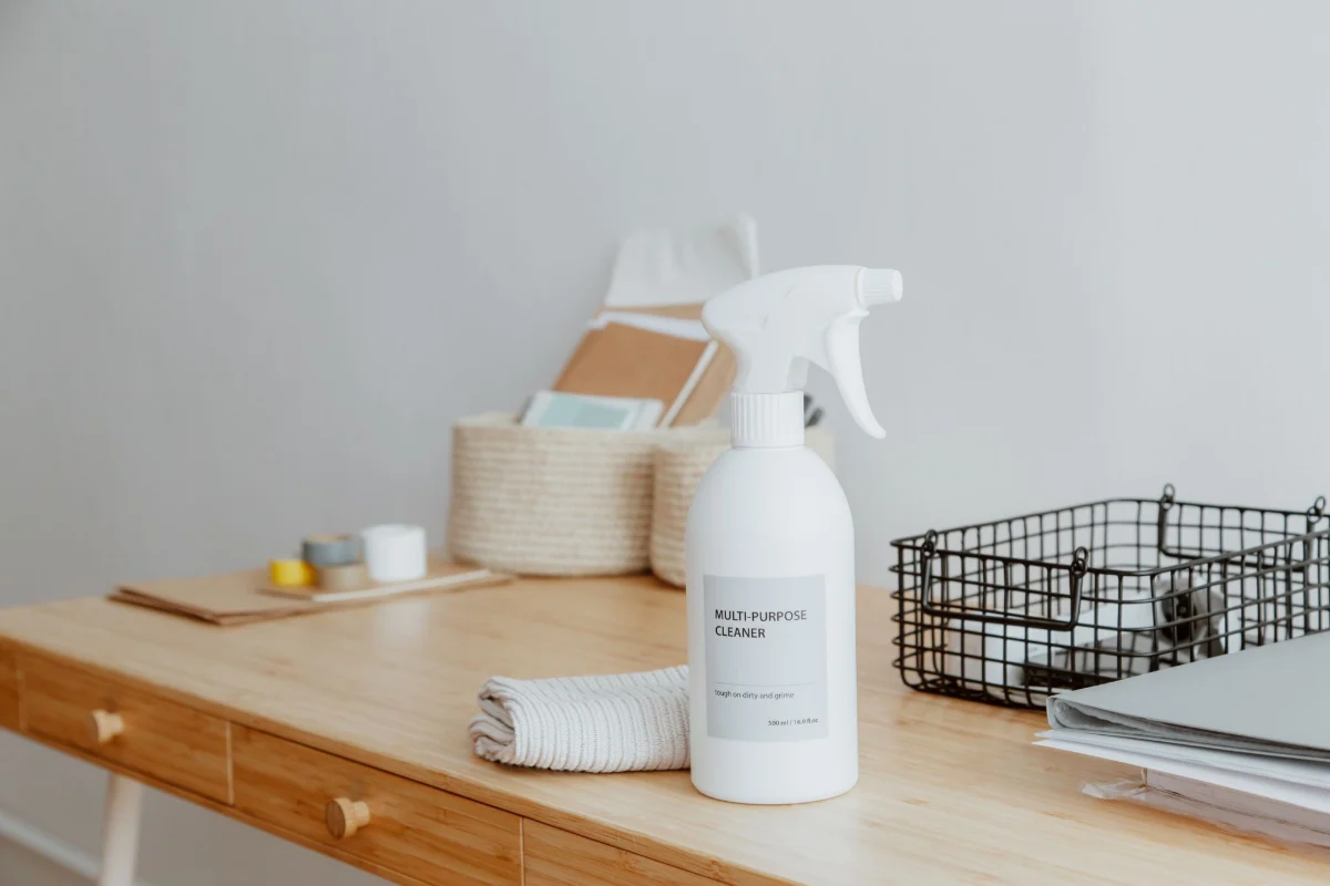 Multi-purpose cleaner spray bottle and a folded towel on a wooden desk