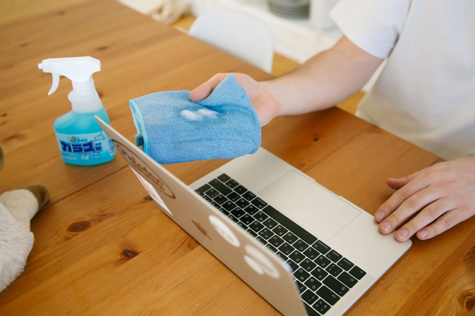 Wiping a laptop with a microfiber cloth and spray cleaner
