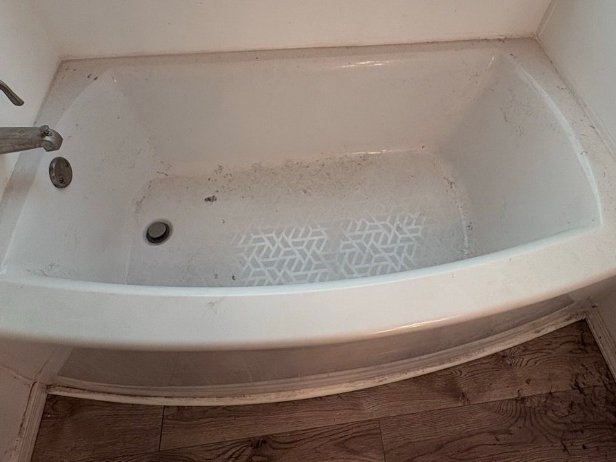 Bathtub with grit and dark specks on the floor and rim before a cleaning in Fort Mohave, AZ