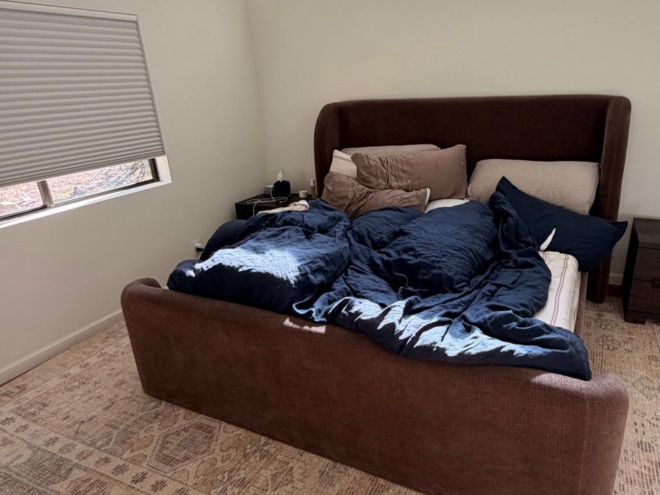 Unmade bed with a rumpled navy duvet in a bright bedroom before a cleaning in Flagstaff, AZ