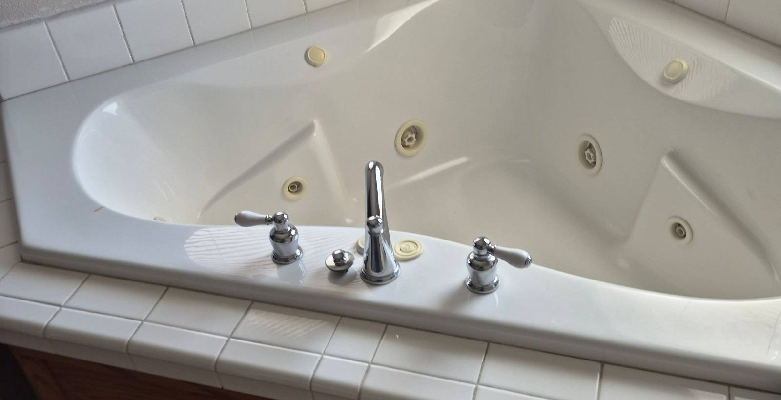 Clean white jetted corner bathtub with shiny chrome fixtures after a cleaning in Bullhead City, AZ