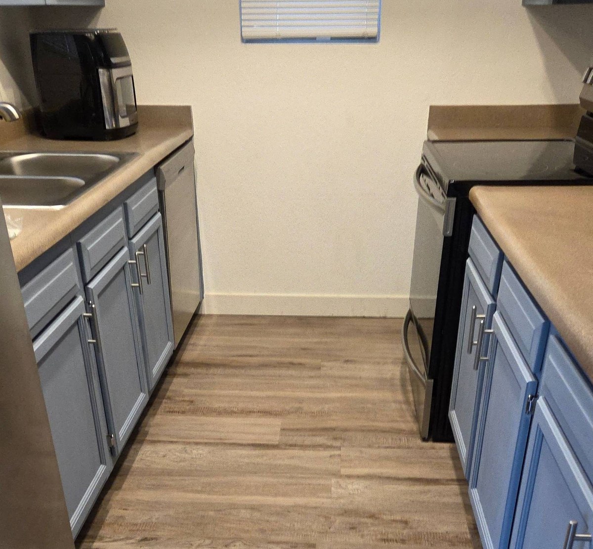Clean galley kitchen with blue gray cabinets, a stainless range, and a wood look plank floor in Tempe, AZ