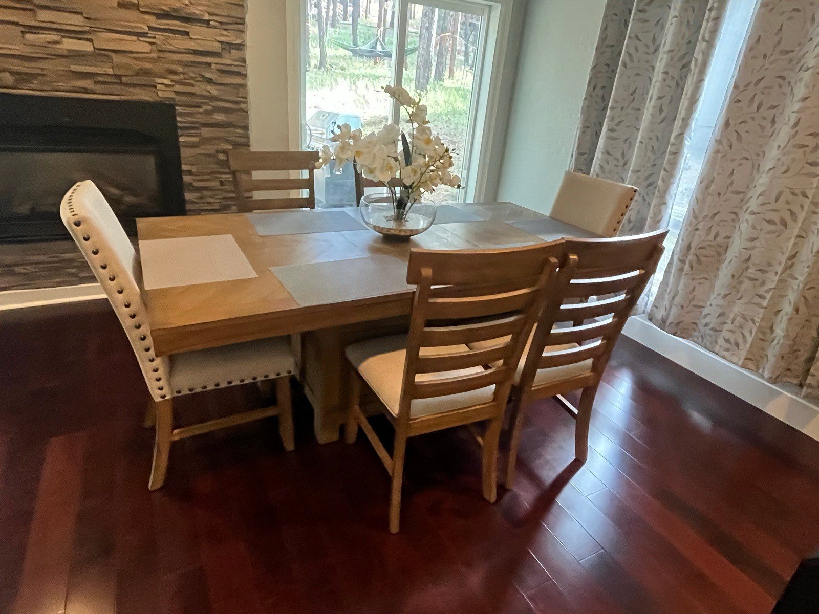 Clean dining table and stone fireplace with pine trees outside the window in a Flagstaff, AZ home