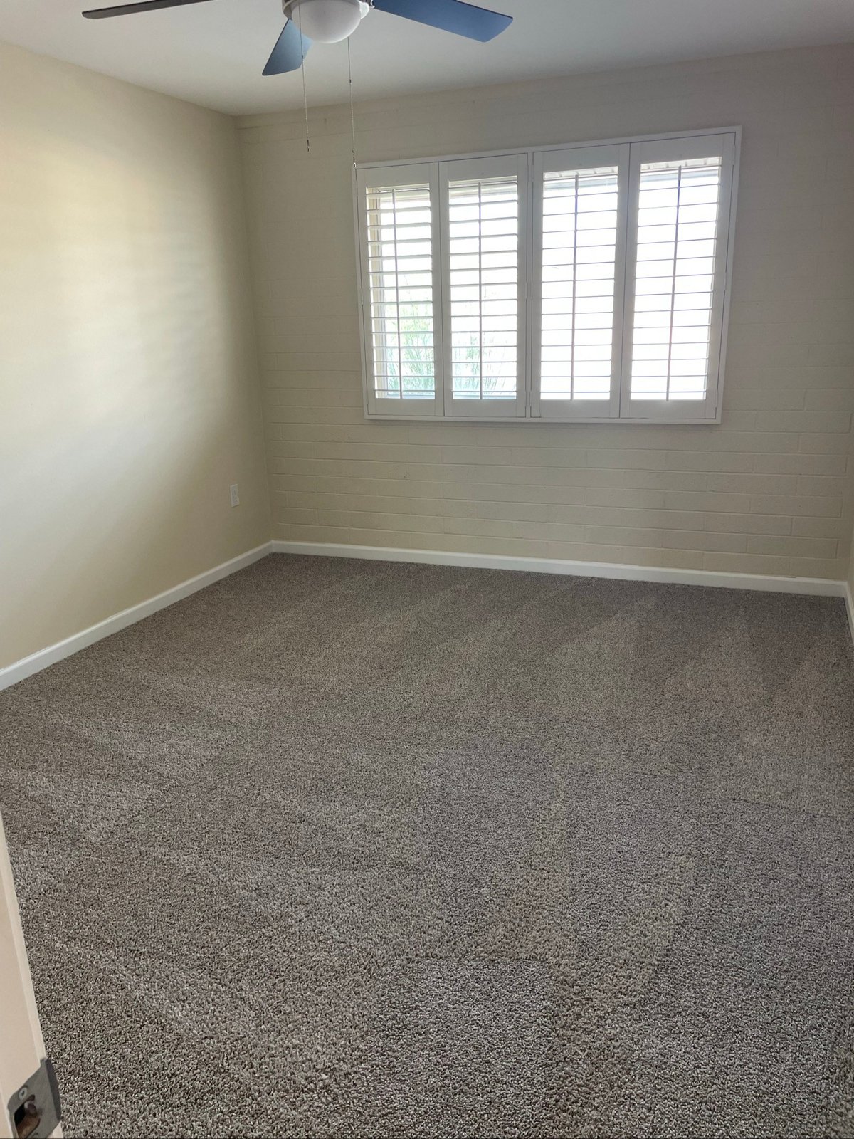 Empty carpeted bedroom with white plantation shutters and a ceiling fan after a house cleaning in Sun City, AZ