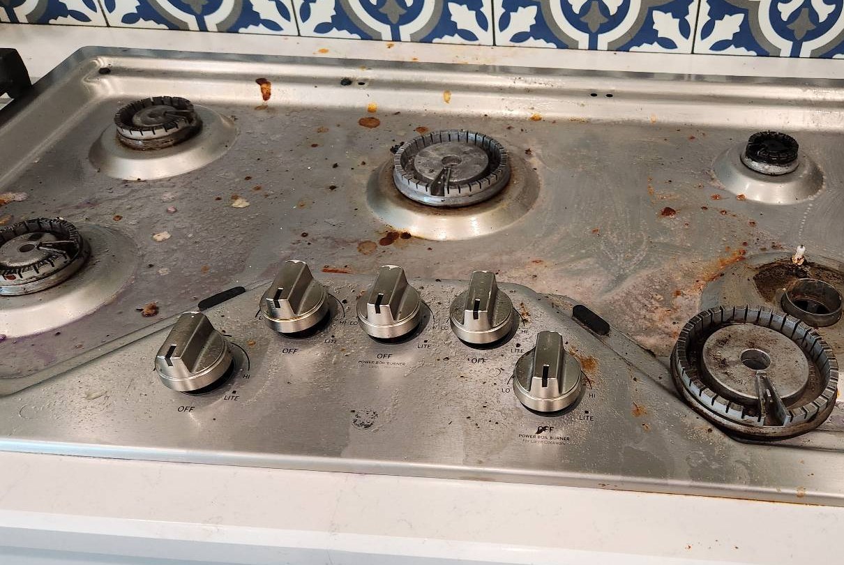Gas stovetop with burnt-on grease and rust-colored splatter before a cleaning in Marana, AZ