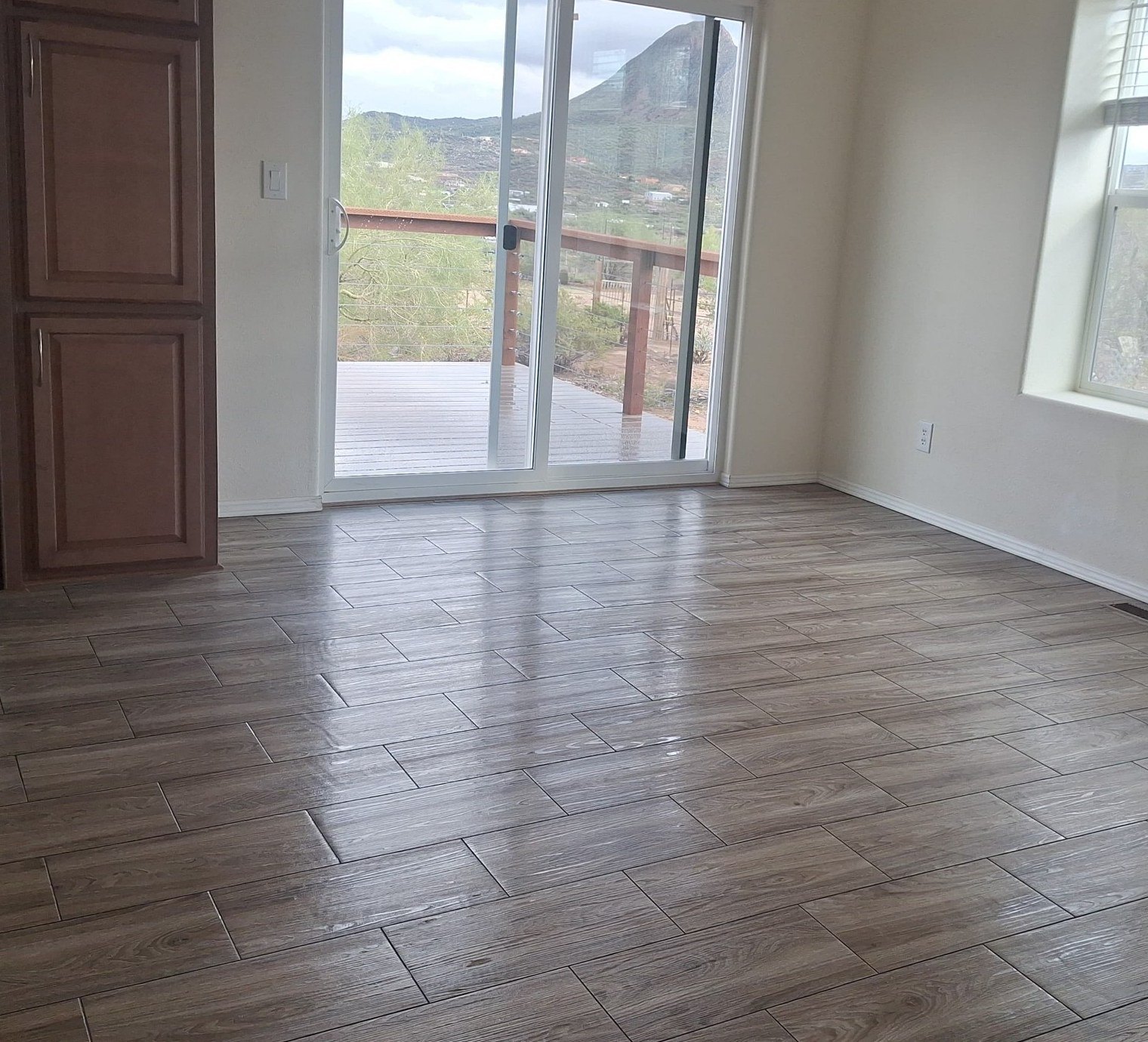 Empty great room with clean wood-look tile floors and a sliding door to a mountain view after a move-out cleaning in New River, AZ