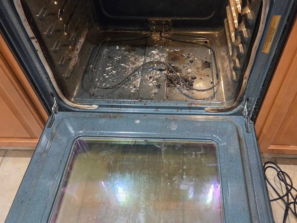 Open oven with burnt-on debris on the floor and greasy door glass before cleaning in Anthem, AZ