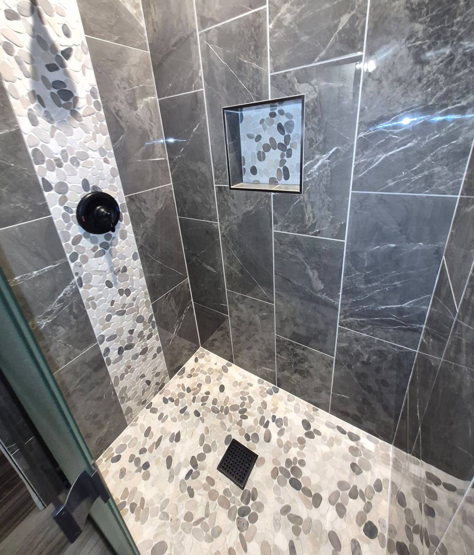 Clean tiled walk-in shower with a pebble floor and black fixtures after a house cleaning in Parker, AZ