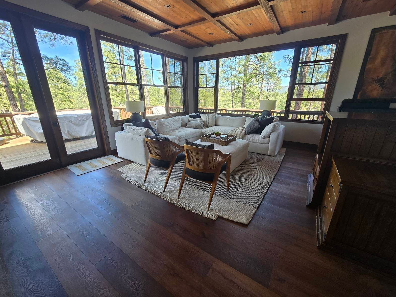 Bright living room with a white sectional, wood floors, and pine trees outside after a cleaning in Payson, AZ