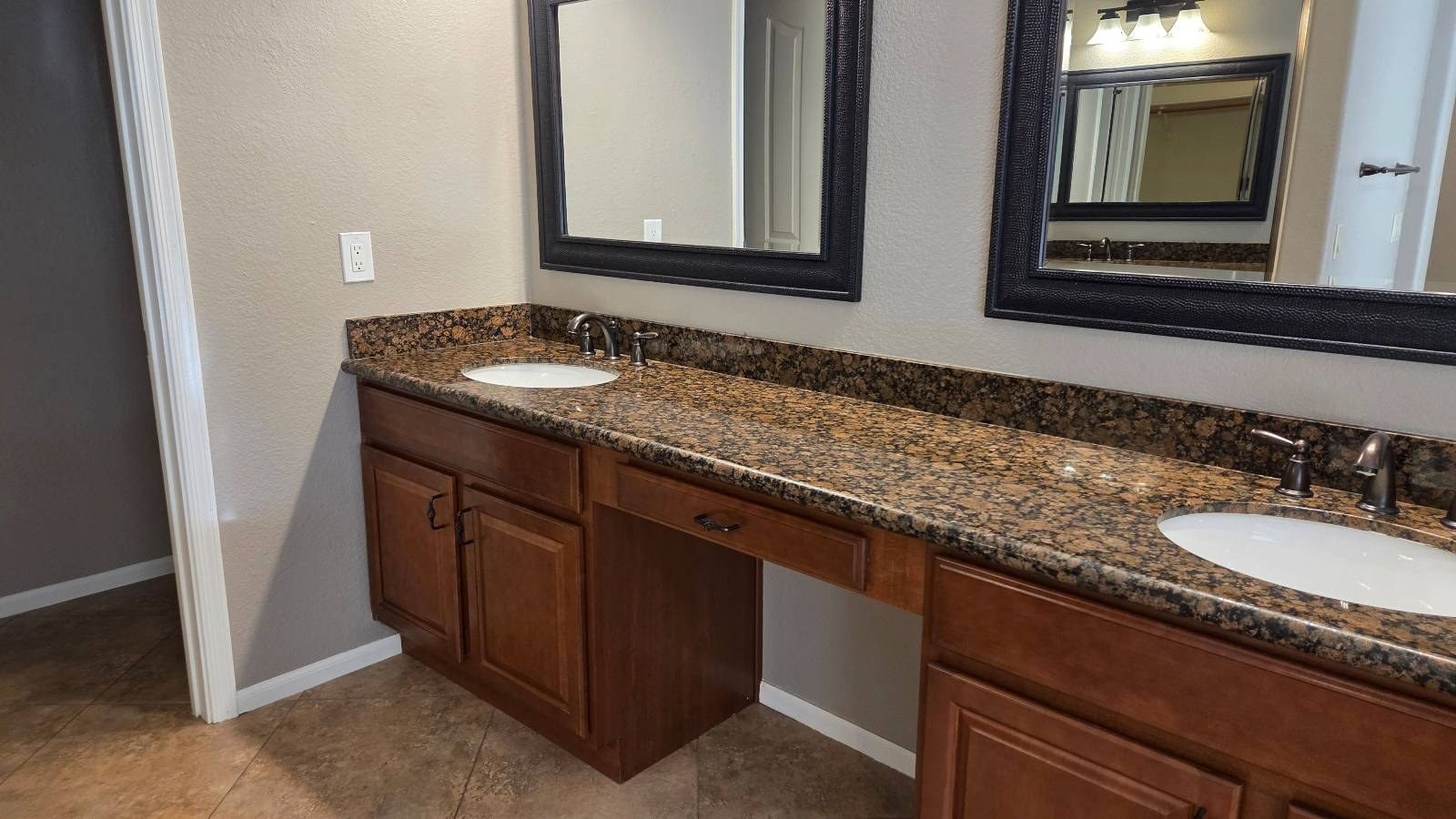 Bathroom vanity with a brown granite counter, two sinks and framed mirrors after a cleaning in Phoenix, AZ
