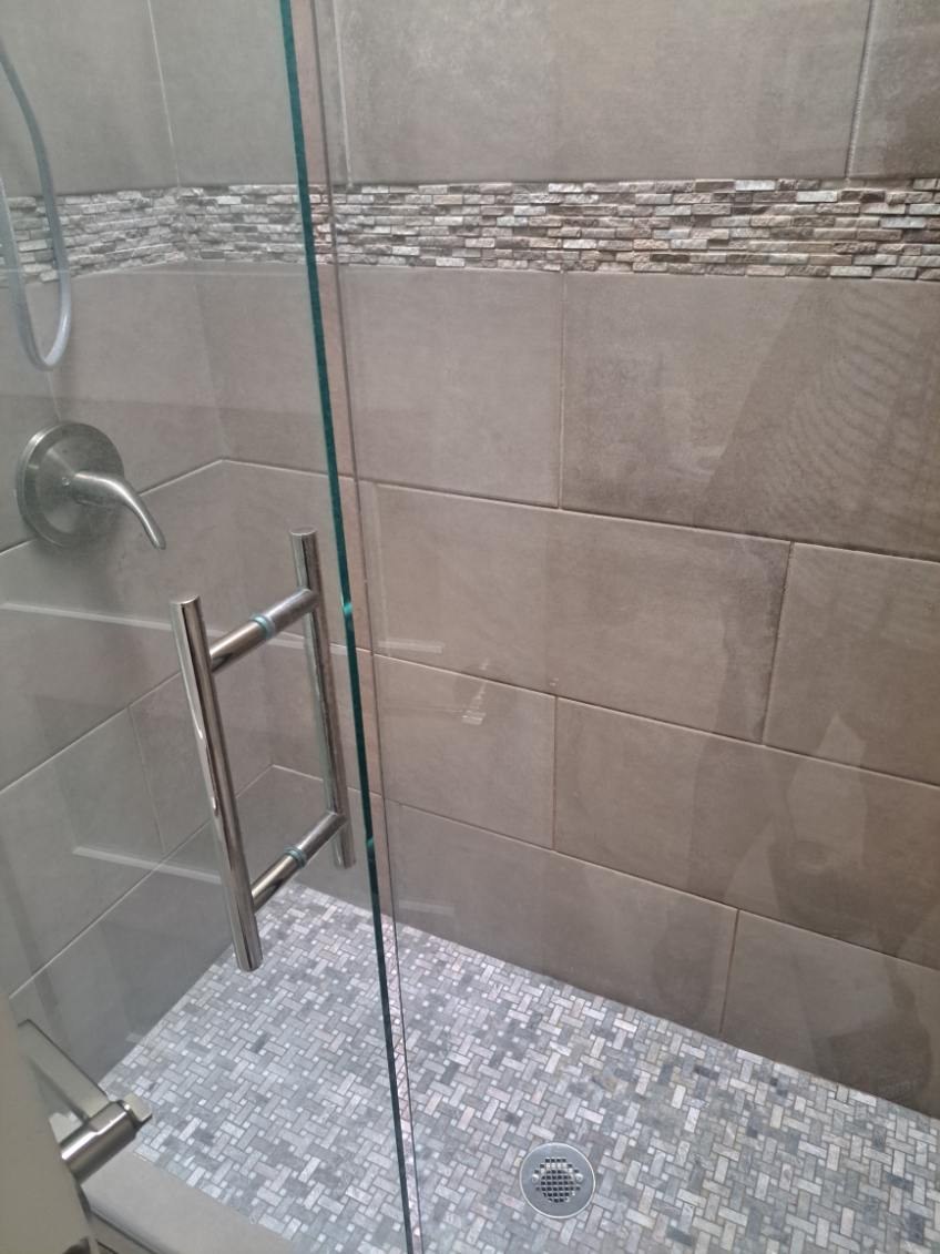 Clean walk-in glass shower with gray tile and a pebble floor after a house cleaning in Sedona, AZ