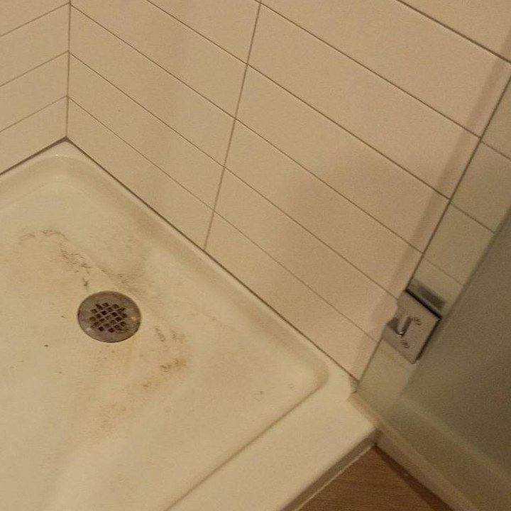 Shower pan with brown stains around the drain before a cleaning in Goodyear, AZ
