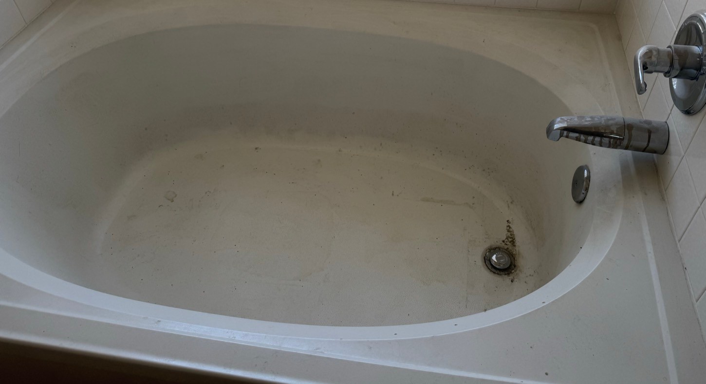Bathtub with a gray film, black debris at the drain, and hard water spots on the faucet before a cleaning in Sierra Vista, AZ