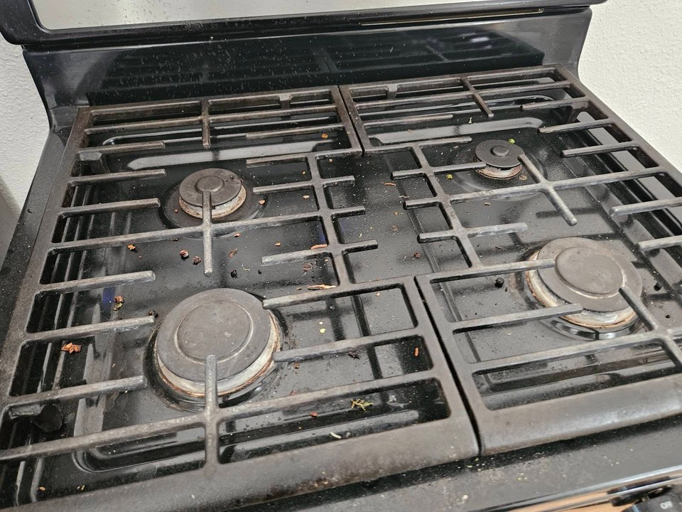 Gas range with crumbs and debris on the grates before cleaning in Tucson, AZ
