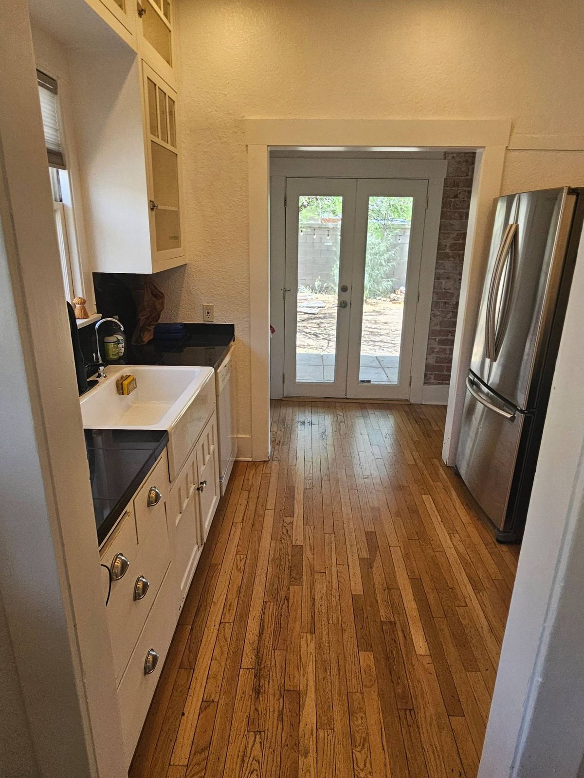 Galley kitchen with white cabinets, black counters, and clean wood floors after a house cleaning in Tucson, AZ
